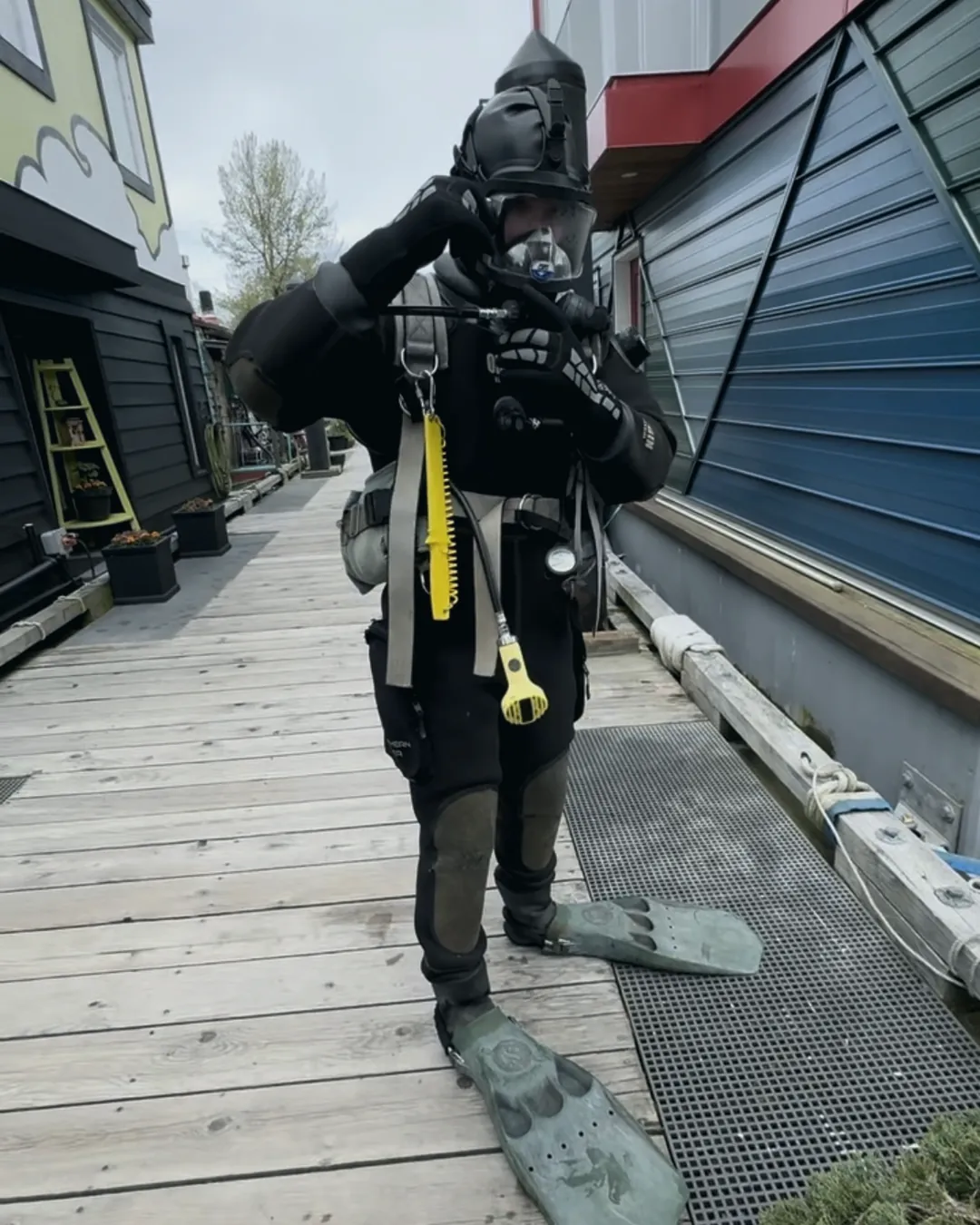 Diver in a drysuit and full face mask walking down a dock with fins